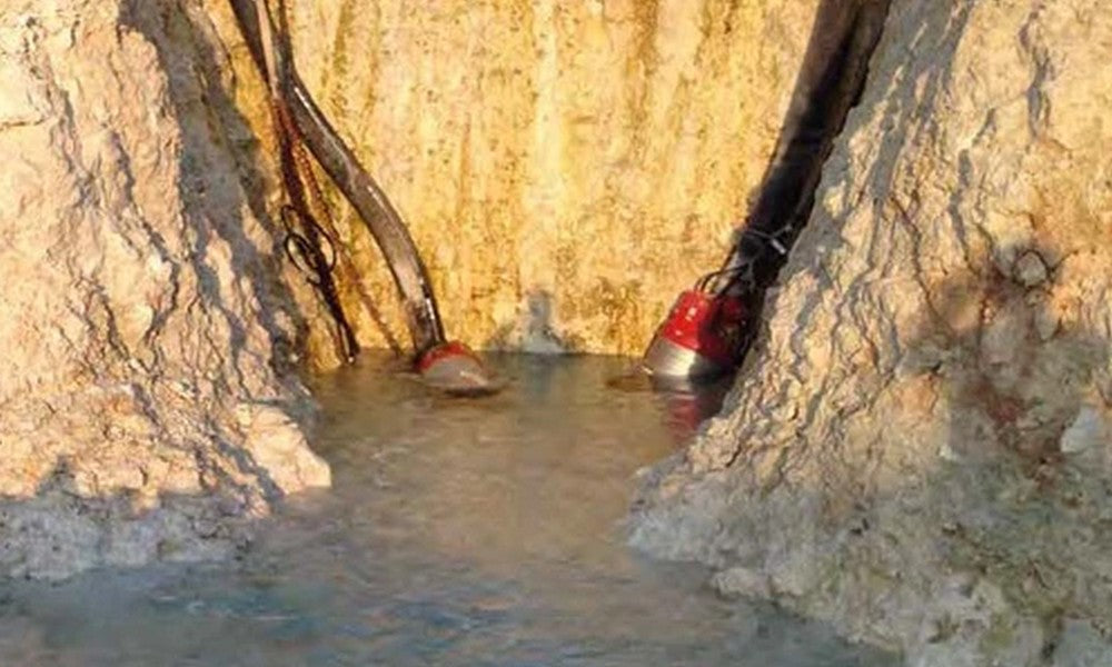 Two red submersible pumps sitting in water and sludge between piles of rock and dirt.