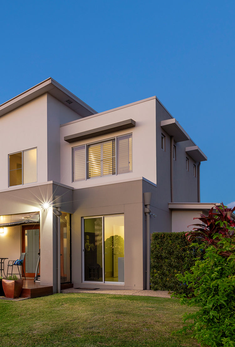 A beige home with windows open and lights on and blue sky in the background.