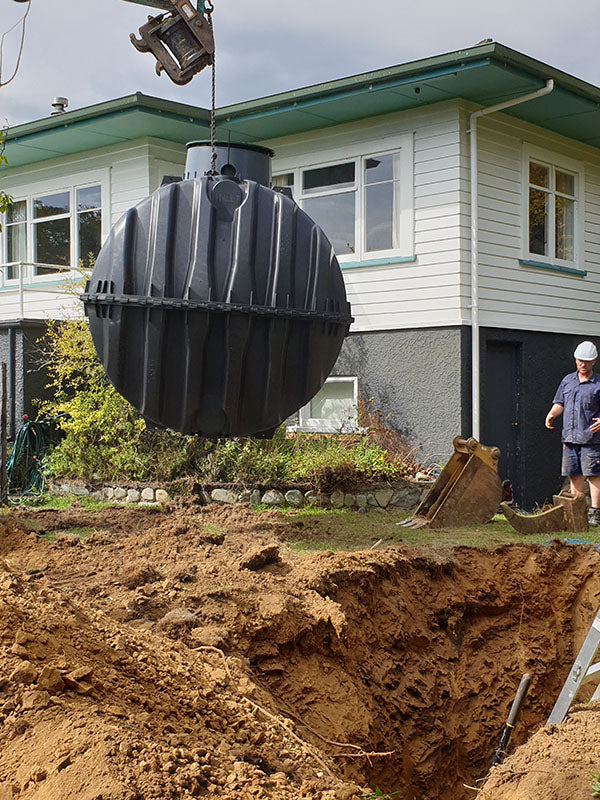 A crane lifting a plastic moulded septic tank into a dirt hole.