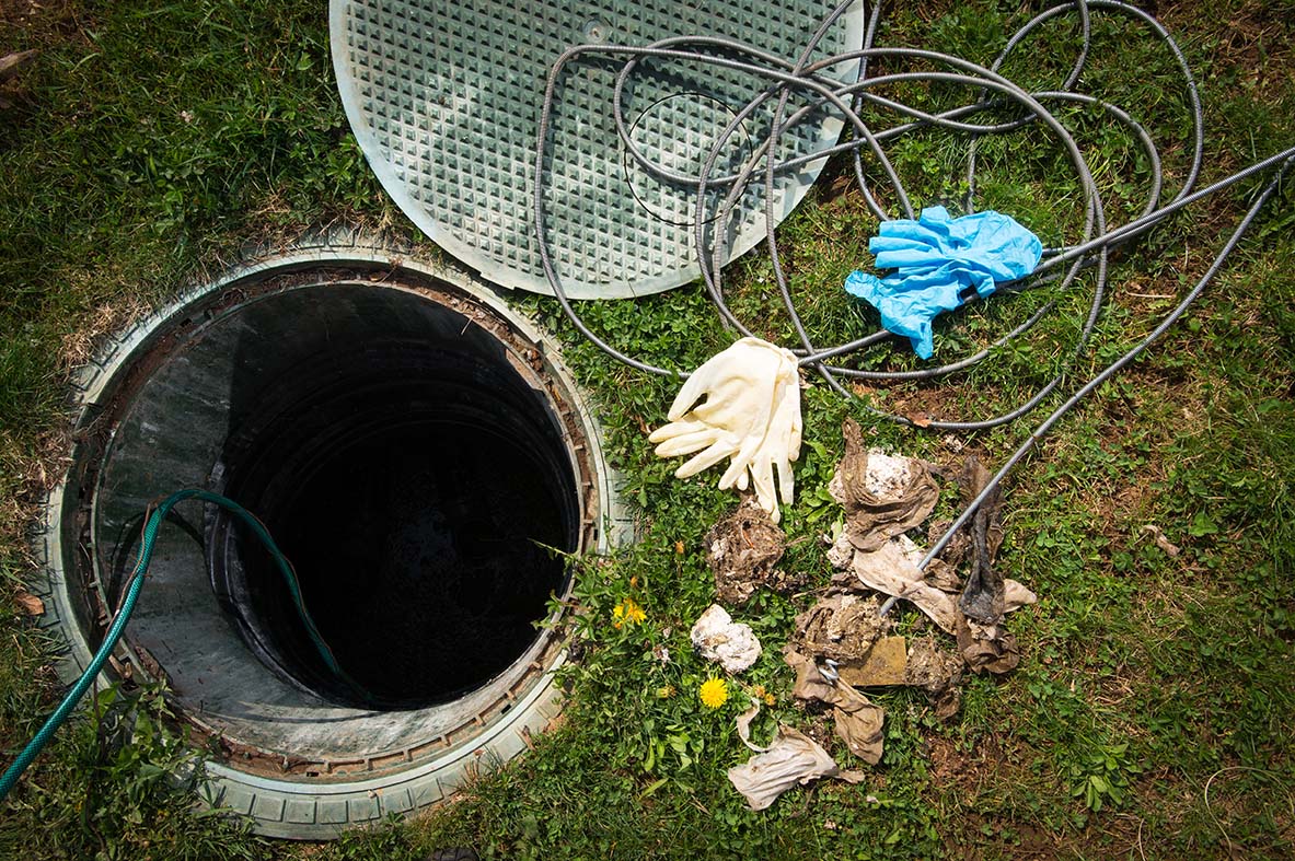 An opened septic tank with cover on the side and a variety of solid materials including gloves to access the sludge inside.