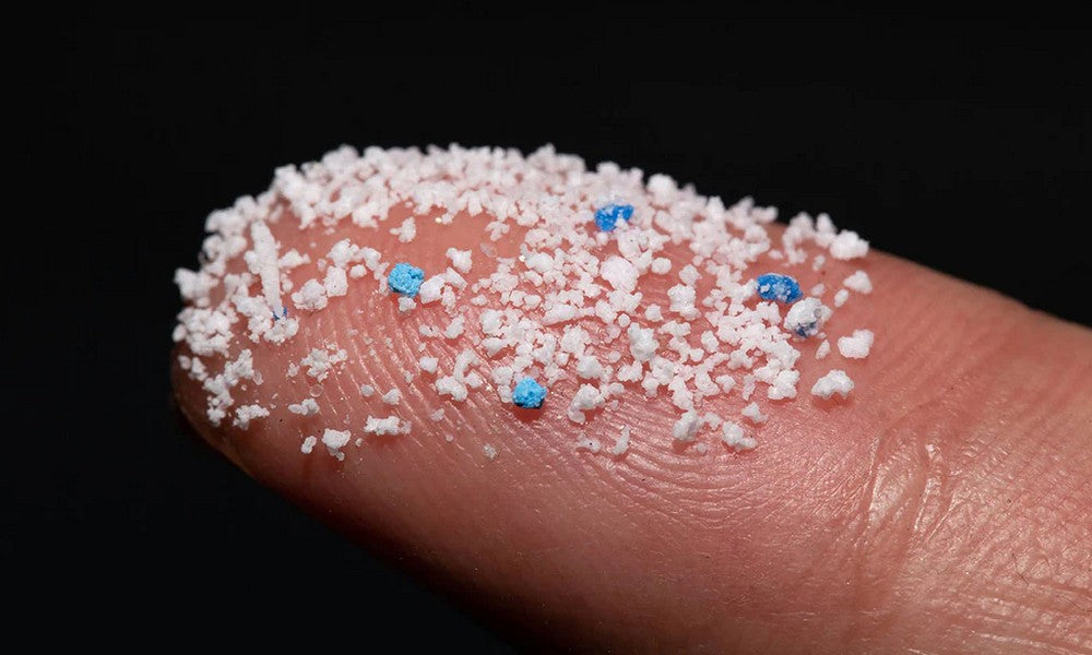 A bunch of white and blue speckles, which are microplastics, sitting on the tip of an index finger.