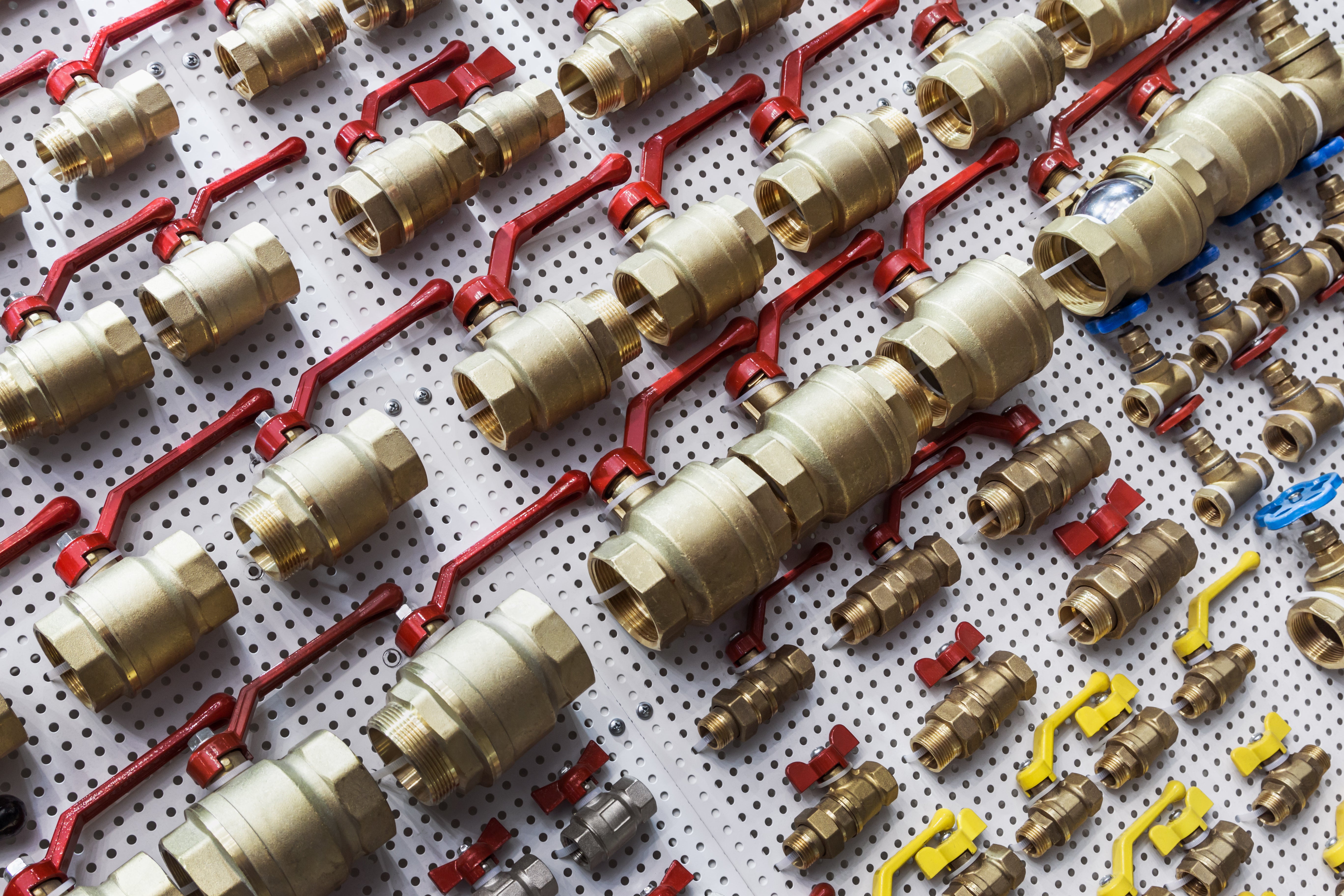 Ball valves with red, yellow, and blue handles displayed on a white peg wall. 